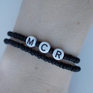 May include: Black beaded bracelet with white letter beads spelling out "MCR".