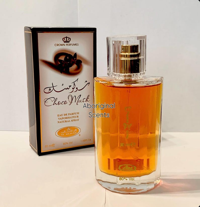 May include: A perfume bottle and box set. The bottle contains a golden-brown liquid and has a clear cap. The box is black with gold accents and features the text "Choco Musk" and "Crown Perfumes". The text "Aboriginal Scents" is also visible.
