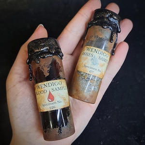 May include: Two small glass vials with dark brown contents and black wax seals. One vial reads "WENDIGO BLOOD SAMPLE" with a red drop graphic and "Specimen No. 226." The other reads "WENDIGO ASHES SAMPLE" and "Specimen No. 477."