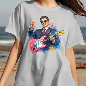 Ronald Reagan graphic on a light gray t-shirt, holding a pink guitar.