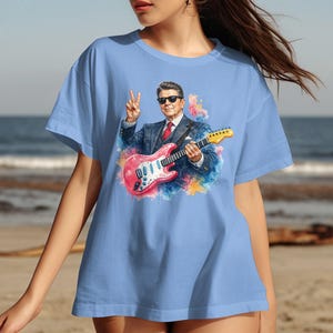 Light blue t-shirt with Ronald Reagan playing a pink guitar.