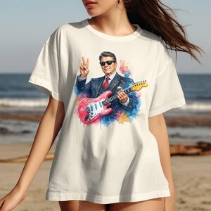 T-shirt featuring Ronald Reagan playing a pink electric guitar and giving peace sign.