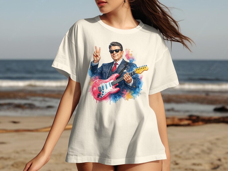T-shirt featuring Ronald Reagan playing a pink electric guitar and giving peace sign.