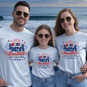 Puede incluir: Tres personas con camisetas azul claro con un dise&ntilde;o patri&oacute;tico. El dise&ntilde;o incluye el texto "AMERICA 250 years of freedom 1776-2026" en rojo, blanco y azul, con fuegos artificiales y estrellas. Est&aacute;n de pie frente a una piscina y el oc&eacute;ano.