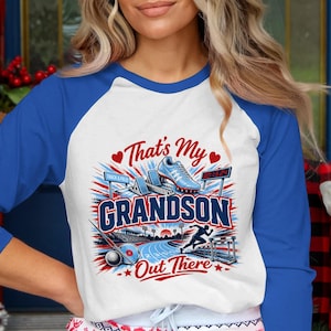 May include: A white and blue raglan baseball tee with the text "That's My Grandson Out There" in a graphic design. The design includes track and field elements like a running shoe, hurdles, and a track.