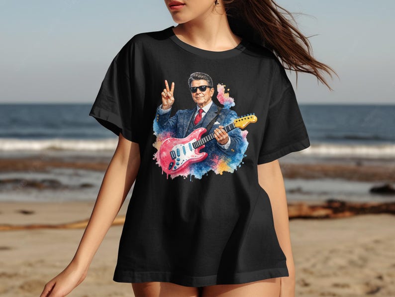 Person wearing black t-shirt with watercolor portrait of guitarist playing pink guitar.