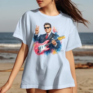 T-shirt with watercolor painting of Ronald Reagan playing guitar on beach.