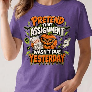 Könnte beinhalten: Ein violettes T-Shirt mit kurzen Ärmeln und einem Aufdruck eines orangefarbenen Kürbisses mit schwarzer Brille, der einen Stapel Papiere mit der Aufschrift LATE hält. Der Text lautet PRETEND THAT ASSIGNMENT WASN'T DUE YESTERDAY, umgeben von Fledermäusen, einem Geist und Totenköpfen.