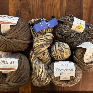 Op de afbeelding: Assortiment van garenklossen in verschillende tinten bruin, beige en grijs. De garenmerken omvatten Galway, Espresso, Providence en Gedifra.
