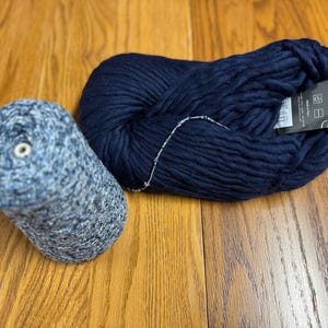 Op de afbeelding: Twee bollen garen, één blauw en één blauw met witte vlekken. De blauwe bol heeft een label met de tekst "Cascade 220 Superwash".