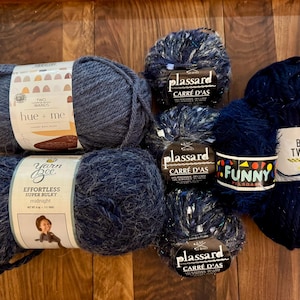 Op de afbeelding: Assortiment van blauwe garenklossen, waaronder twee klossen Yarn Bee Effortless Super Bulky Midnight, twee klossen Plassard Carré d'As en één klos Big Twist Funny.