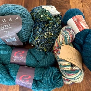 Op de afbeelding: Assortiment van teal garenklossen, waaronder Rowan Big Wool 100g, Ella Rae Super Alpaca en Mirasi Serpentima handgeverfd garen.
