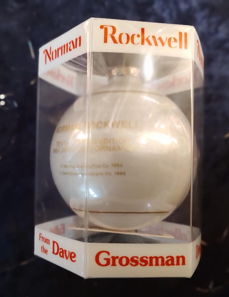 May include: A white glass Christmas ornament with gold lettering that reads "Norman Rockwell Edition Ornament". The ornament is in a clear plastic box with a red label that reads "Rockwell" and "Grossman".