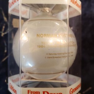 May include: A white glass Christmas ornament with gold lettering that reads "Norman Rockwell 1984 The Christmas Ornament Edition From Dave Grossman Designs Inc."
