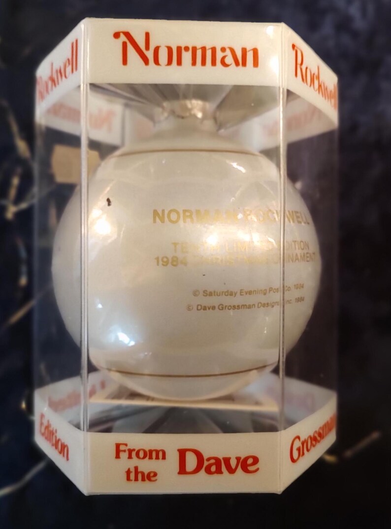 May include: A white glass Christmas ornament with gold lettering that reads "Norman Rockwell 1984 The Christmas Ornament Edition From Dave Grossman Designs Inc."