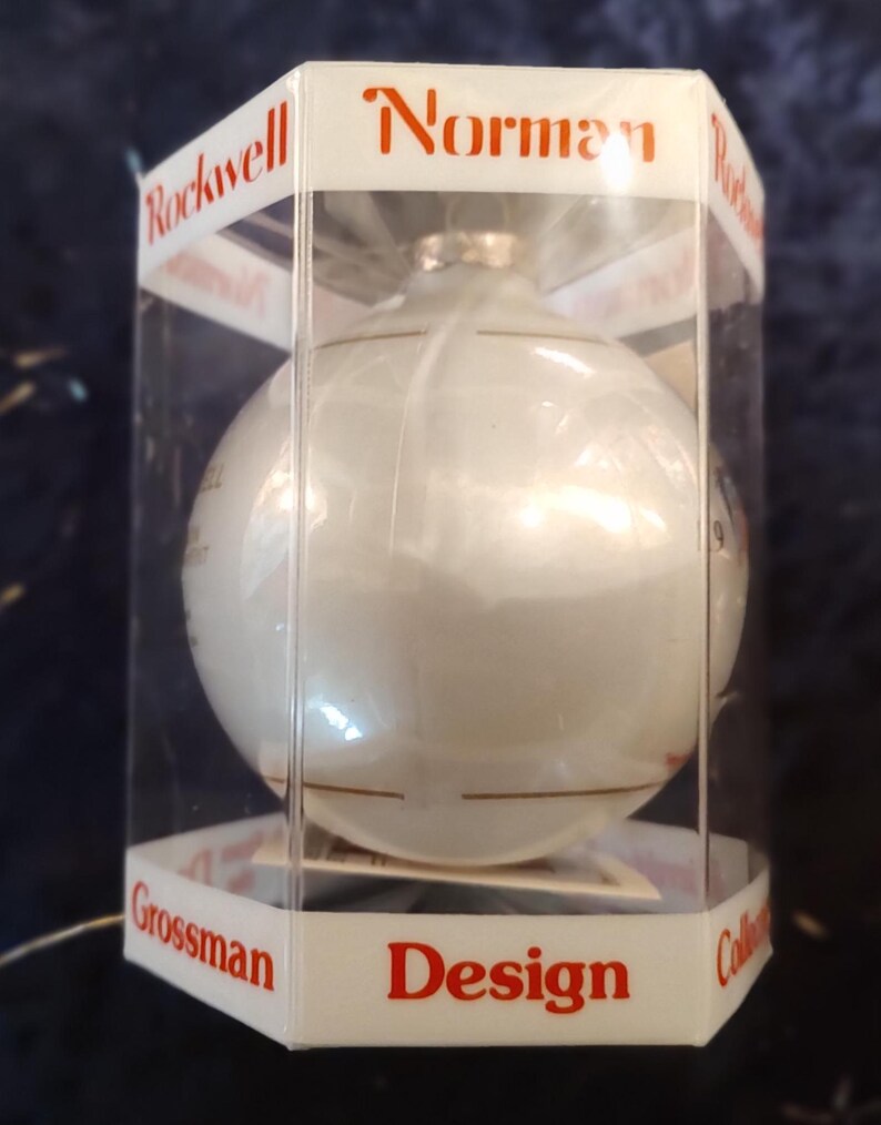 May include: A white glass Christmas ornament with gold trim in a clear plastic box. The box has the words "Norman Rockwell Grossman Design Collection" printed on it.