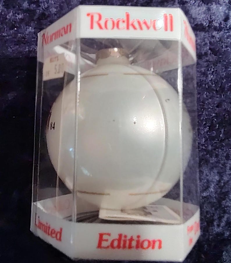 May include: A white glass Christmas ornament with a gold trim, in a clear plastic box. The box has the words "Rockwell" and "Limited Edition" printed on it.
