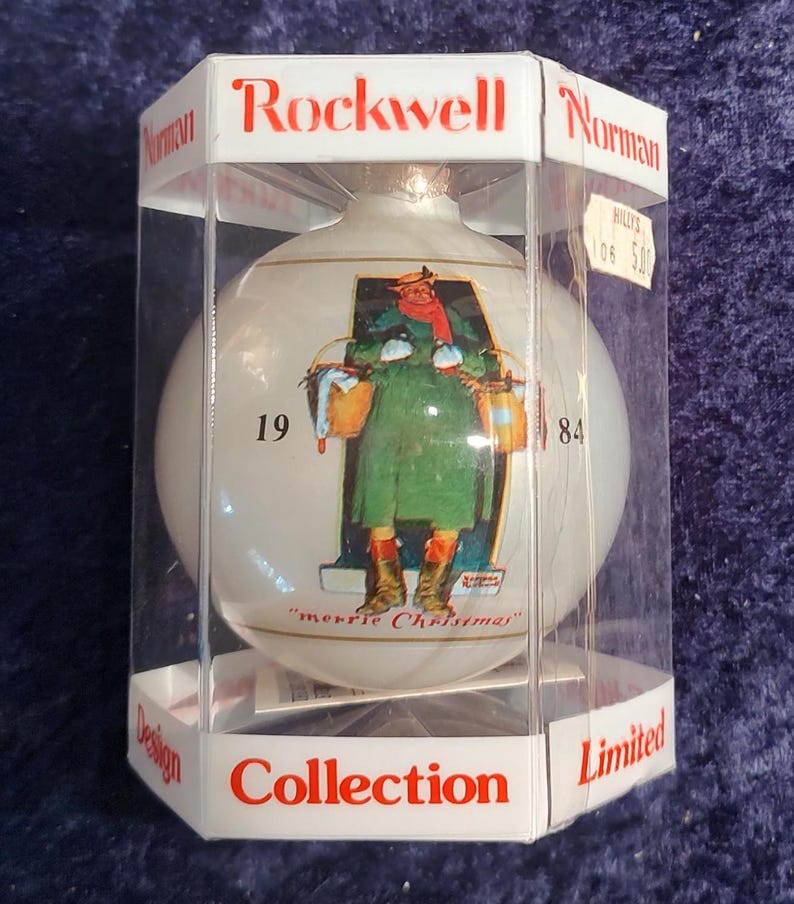 May include: A white glass Christmas ornament with a Norman Rockwell illustration of a woman carrying a basket of gifts. The ornament is in a clear plastic box with a red label that says "Rockwell Collection Limited".