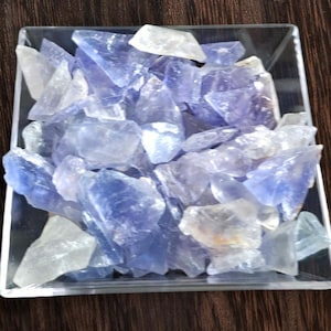 May include: A clear square glass container filled with a collection of blue and white crystal shards. The crystals vary in size and shape, with a translucent quality. The crystals are a mix of light blue and clear, creating a visually appealing display.
