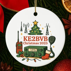 May include: White ceramic Christmas ornament with a festive design. It features a green Christmas tree, radio equipment, and the text "KE2BVB Christmas 2025". The ornament is decorated with a red stocking and a microphone.
