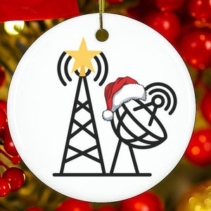 May include: White ceramic Christmas ornament with a black and yellow graphic of a radio tower, a satellite dish, and a star. The satellite dish has a Santa hat. The ornament hangs from a gold string.