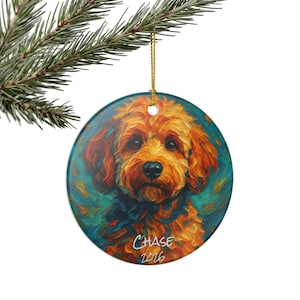 May include: A round ceramic ornament featuring an impressionistic painting of a golden-brown dog with curly fur against a teal background. The name Chase and the year 2026 are printed in white script at the bottom. It hangs from a gold string.