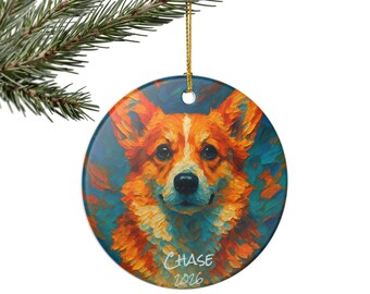 May include: A round ceramic ornament featuring an impressionistic painting of a Corgi dog with orange and white fur against a blue background. The name CHASE and the year 2026 are printed in white text at the bottom. It hangs from a gold string.