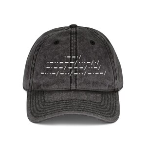May include: A charcoal black baseball cap with a distressed, washed-out finish. The front panel features white embroidered Morse code symbols arranged in three distinct lines, centered above the curved brim with matching stitching details.