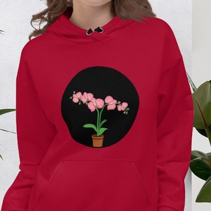 Puede incluir: Sudadera con capucha roja con un gráfico circular negro que presenta una planta de orquídea rosa en una maceta marrón.