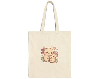 May include: A cream-coloured tote bag with a cartoon illustration of two axolotls embracing, and a small pink heart above them. The axolotls are light yellow with pink gills and green accents. The bag has long handles and a simple design.