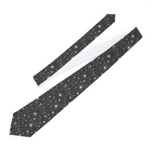 May include: A necktie featuring a dark charcoal grey background with a repeating pattern of gold-coloured stars and small white dots. The tie has a pointed tip and a white lining visible on the underside of the folded fabric section.