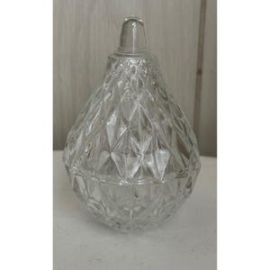 May include: A clear glass lidded jar shaped like a pear, featuring a textured diamond-cut pattern across its surface. The container has a rounded base and a tapered top section that culminates in a smooth, rounded finial handle on the lid.