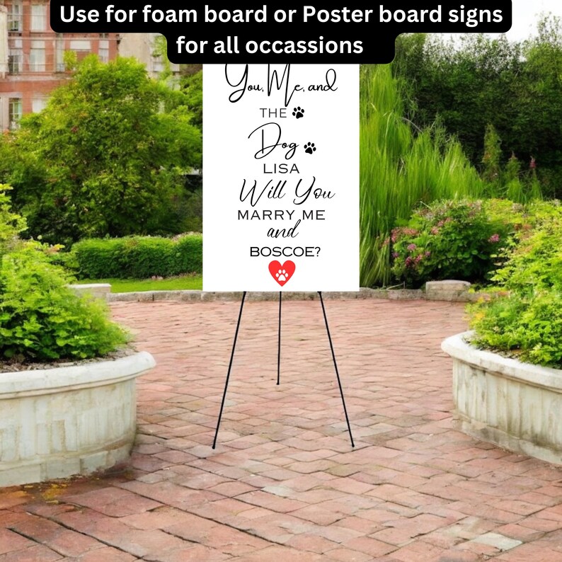 May include: A white foam board sign on a black easel, with the text "You, Me, and THE Dog LISA Will You MARRY ME and BOSCOE?" and a red heart with a paw print. The sign is for all occasions.