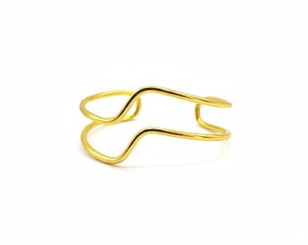 May include: A gold-colored, open cuff bracelet with a unique, wavy design. The bracelet features two parallel, curved bands that create an open, minimalist style. The jewelry is set against a white background.