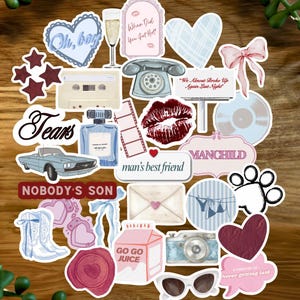 Peut inclure: Une collection d'autocollants décoratifs avec divers motifs, notamment des cœurs, une cassette, un flacon de parfum, une voiture et des textes tels que "Tears" et "Nobody's Son". Les autocollants sont disposés sur une surface en bois.
