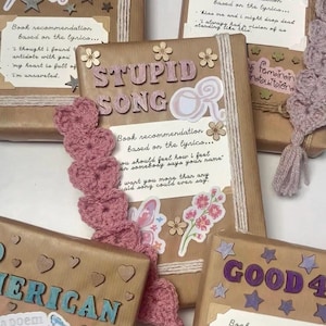 Könnte beinhalten: Mehrere in braunes Papier eingewickelte Bücher, verziert mit hölzernen Sternen, Herzen und Blumen. Jedes Buch hat einen Titel aus ausgeschnittenen Buchstaben, einen Aufkleber und eine weiße Karte mit Liedtexten und Buchempfehlungen.