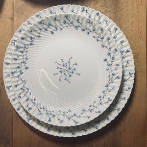 May include: A set of three white ceramic plates with a blue floral pattern. The plates are nested together and have a scalloped edge.