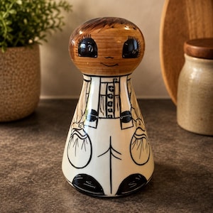 Può includere: Statuina vintage in ceramica con testa in legno e corpo dipinto. La statuina ha un viso sorridente con grandi occhi ed è vestita con un abito bianco e nero. La statuina è alta circa 15 cm.