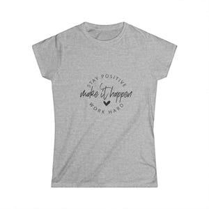 May include: A heather gray short-sleeve t-shirt featuring a circular black graphic on the chest. The text reads "STAY POSITIVE" at the top, "make it happen" in the center, and "WORK HARD" at the bottom, with a small black heart icon below the text.