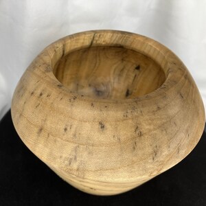 May include: A handcrafted wooden bowl with a unique, organic shape. The bowl is made from light-colored wood with dark speckles, showcasing the natural grain. The interior is smooth, and the exterior has a slightly rough texture. This decorative bowl is perfect for holding small items.