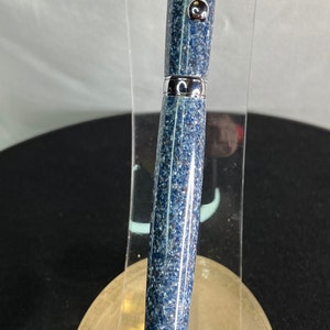 May include: A blue and silver pen with a speckled design. The pen has a silver clip and tip, and is displayed on a clear acrylic stand. The pen's body is a speckled blue color.