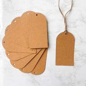 May include: A set of ten brown paper gift tags with holes punched at the top. The tags are arranged in a fan shape. One tag is attached to a piece of twine.