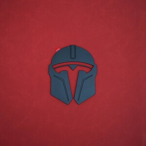 May include: A black Mandalorian helmet design with red accents, set against a red background. The helmet features a distinctive T-shaped visor and angular lines, with a small red detail at the top. The design is a stylized representation of the iconic helmet.