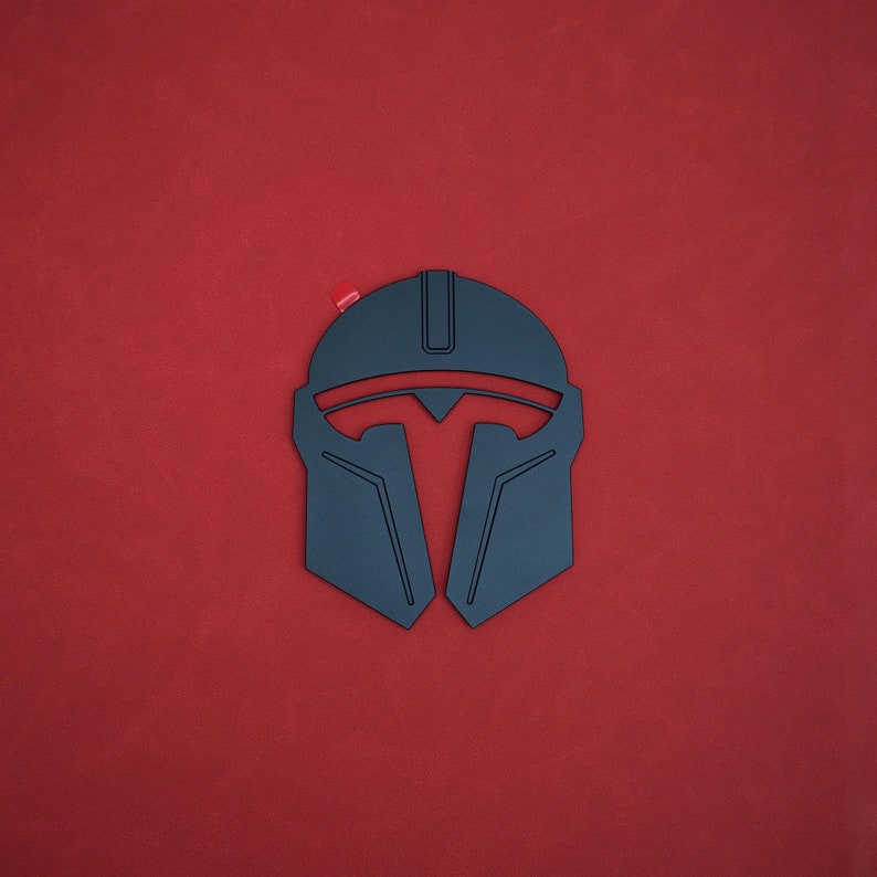 May include: A black Mandalorian helmet design with red accents, set against a red background. The helmet features a distinctive T-shaped visor and angular lines, with a small red detail at the top. The design is a stylized representation of the iconic helmet.