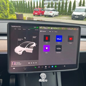 K&ouml;nnte beinhalten: Ein Tesla Model Y Touchscreen-Display, das eine Vielzahl von Apps zeigt, darunter Netflix, Disney+, YouTube, Twitch, Tesla Tutorials und einen Musikplayer. Der Bildschirm zeigt auch eine Karte mit einer geplanten Route und ein Autosymbol, das die Position des Fahrzeugs darstellt.