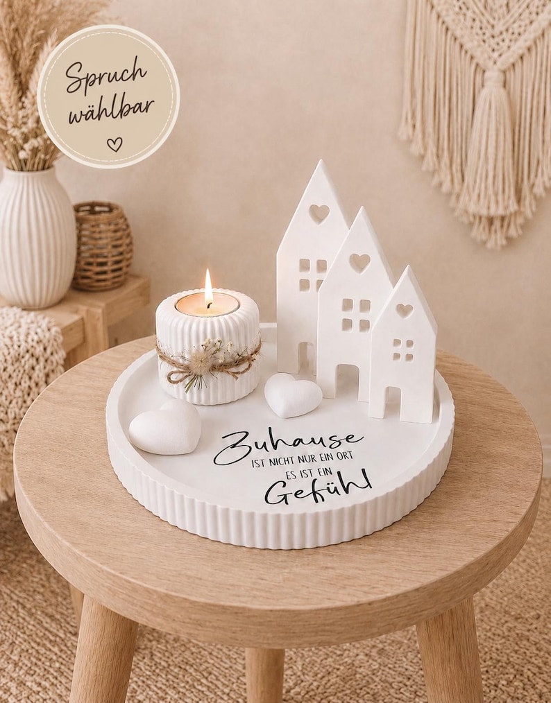 Puede incluir: Una bandeja de cer&aacute;mica blanca con un portavelas, tres decoraciones en forma de casa y dos decoraciones en forma de coraz&oacute;n. La vela est&aacute; encendida. La bandeja tiene el texto "Zuhause ist nicht nur ein Ort es ist ein Gef&uuml;hl".