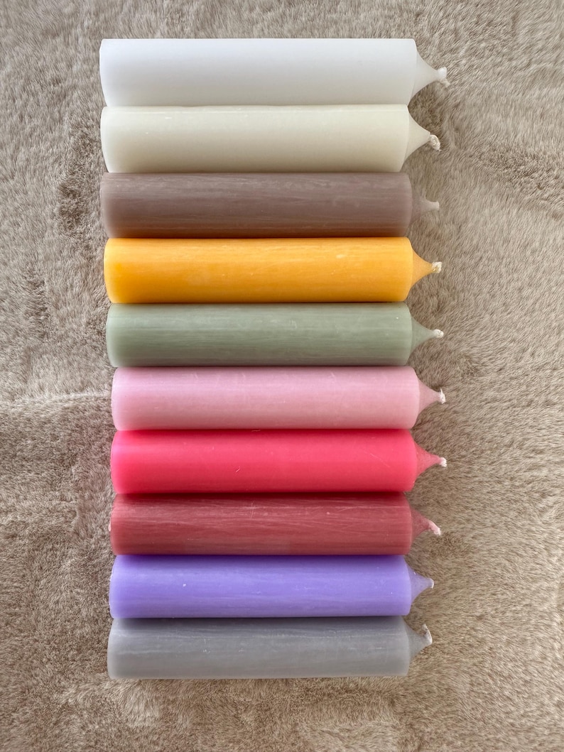 K&ouml;nnte beinhalten: Eine Sammlung von zehn farbigen Stabkerzen in verschiedenen Farbt&ouml;nen, darunter Wei&szlig;, Beige, Braun, Gelb, Gr&uuml;n, Rosa, Rot, Burgunder, Lila und Grau. Die Kerzen sind vertikal angeordnet und zeigen ihre zylindrische Form und ihre Spitzen.