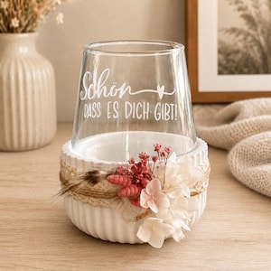 May include: A clear glass tumbler featuring the white text "Sch&ouml;n DASS ES DICH GIBT!" with a small heart icon. The glass sits inside a white, ribbed ceramic bowl decorated with a jute twine wrap, dried pink flowers, and white hydrangea petals.