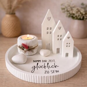 May include: A white decorative tray with a lit candle, ceramic houses, and heart-shaped stones. The houses have heart-shaped cutouts. The tray features the text "Nimm dir Zeit. gl&uuml;cklich ZU SEIN."