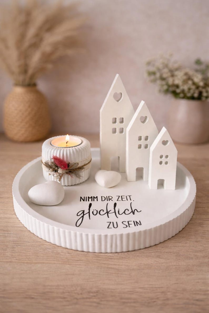 May include: A white decorative tray with a lit candle, ceramic houses, and heart-shaped stones. The houses have heart-shaped cutouts. The tray features the text "Nimm dir Zeit. gl&uuml;cklich ZU SEIN."